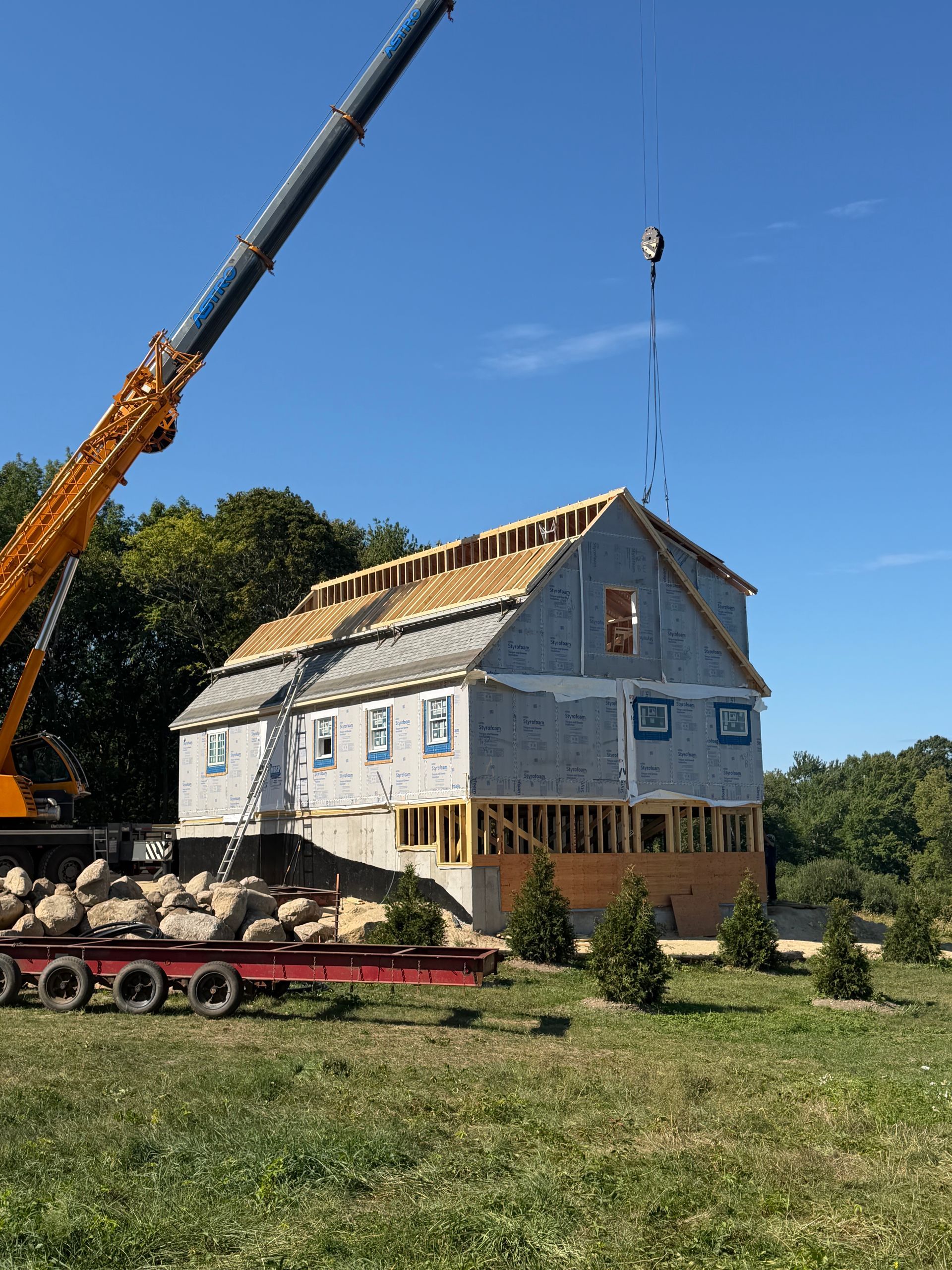 House under construction with crane lifting materials on a grassy site under a blue sky