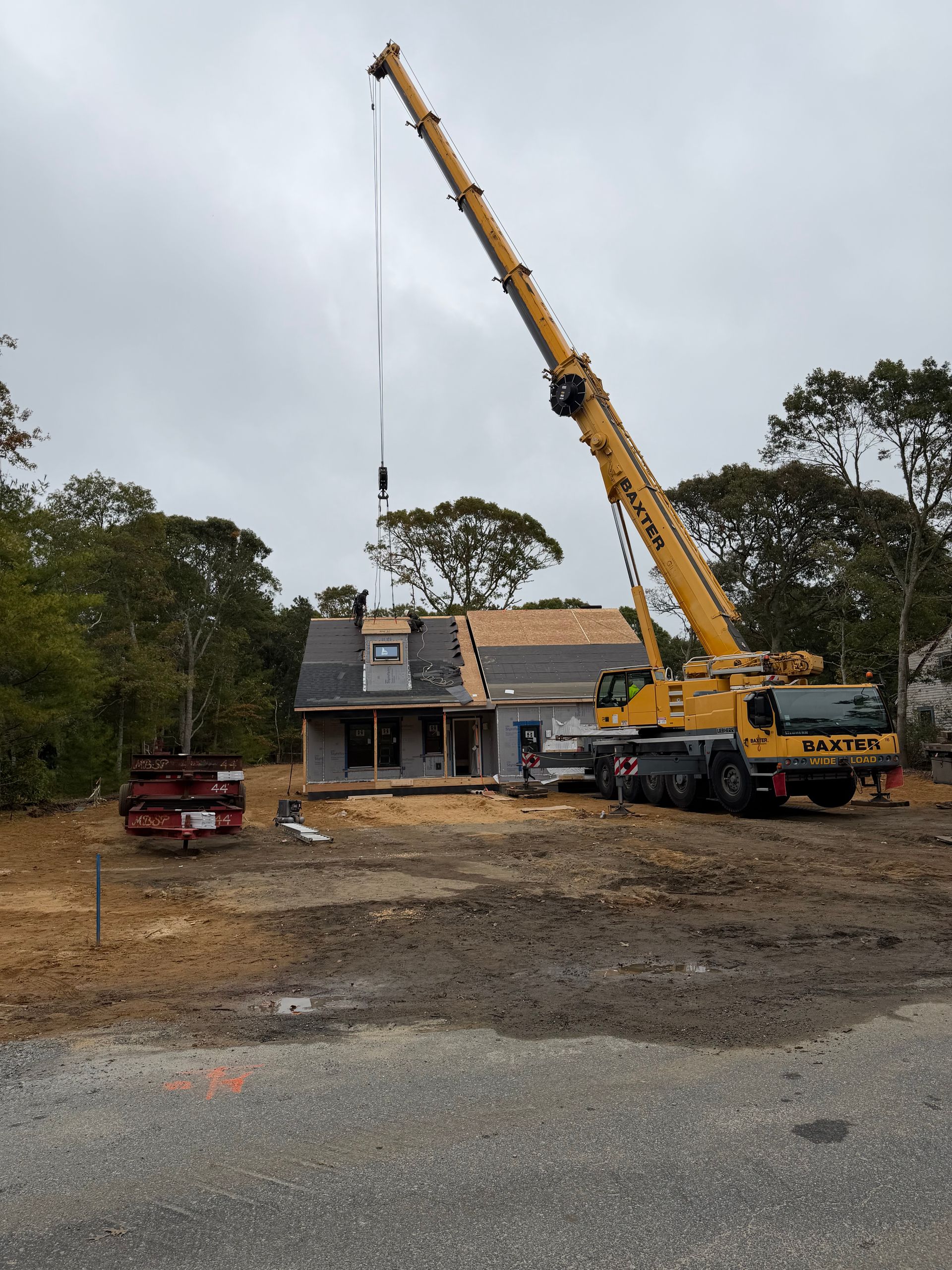 Yellow crane lifting debris over a house under repair, with a red truck and trees nearby