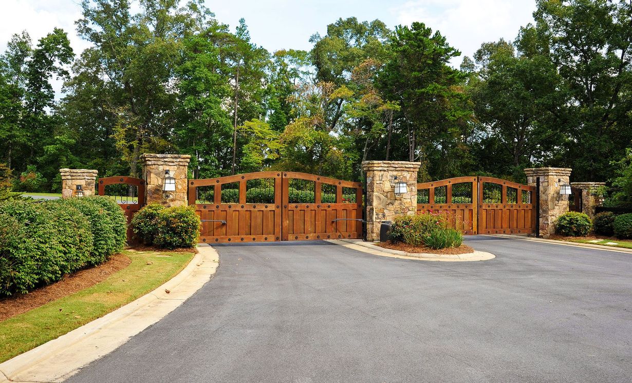 A wooden gate is surrounded by stone pillars on the side of a road.