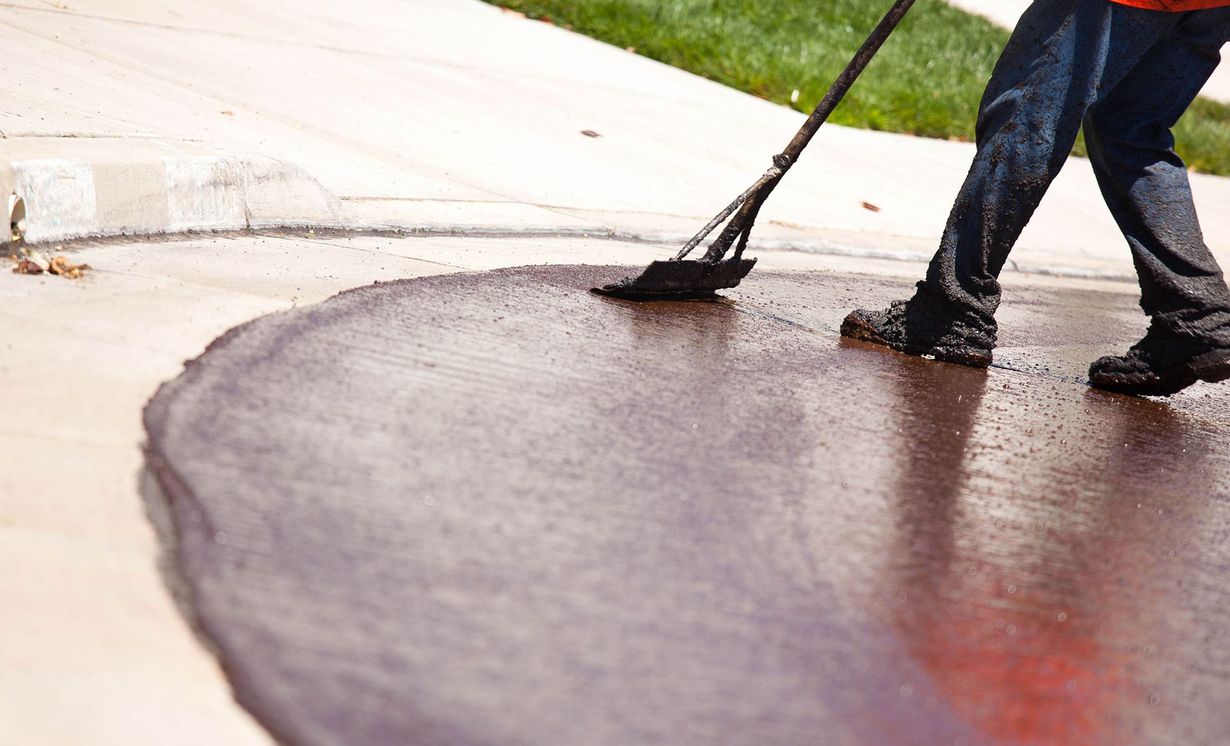 A person is spreading a brown liquid on a concrete surface with a broom.