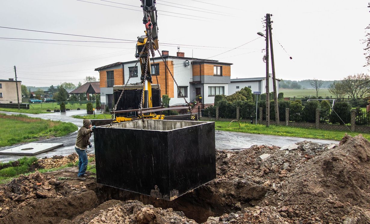 A crane is lifting a concrete block into the ground in front of a house.