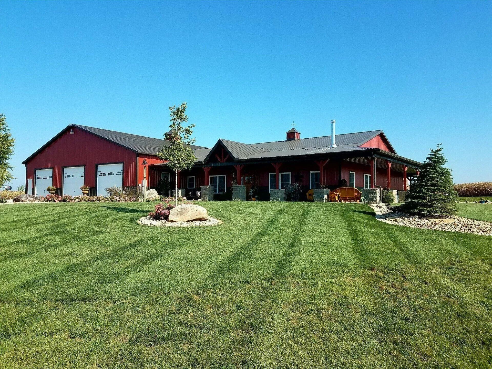 Red barn-style house with garage, on green lawn under a blue sky.