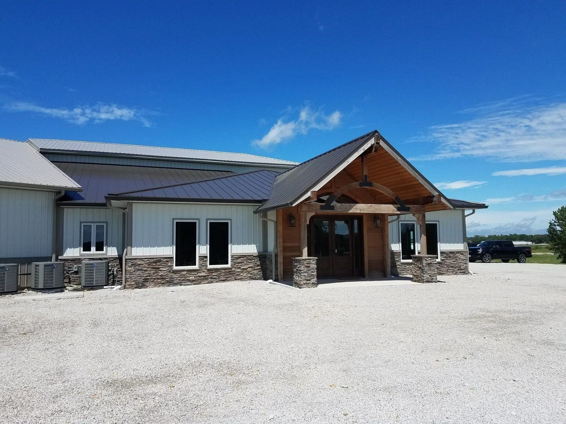 Building with a stone and wood entrance under a blue sky and gravel yard.