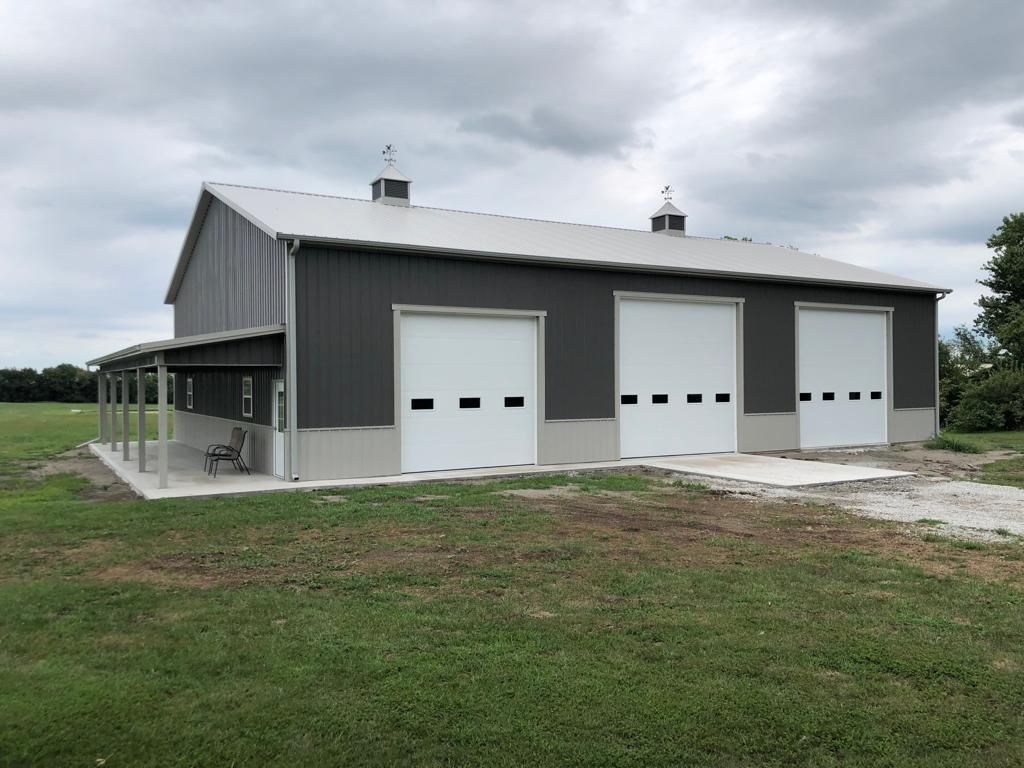 Dark gray metal building with three garage doors and a porch.