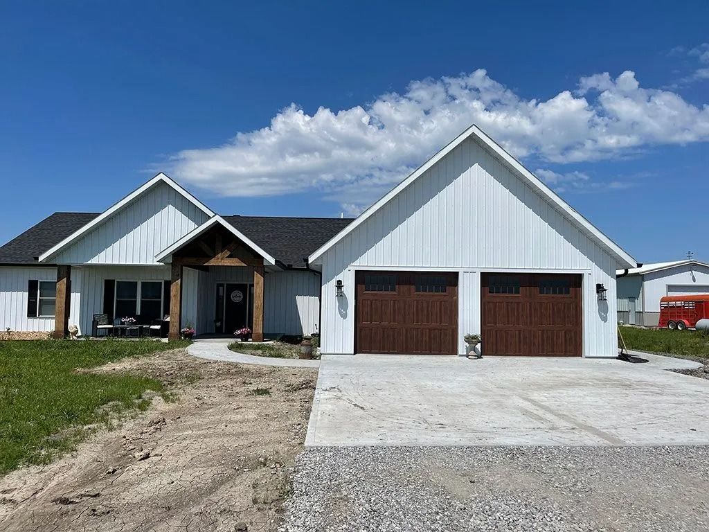 White farmhouse with brown garage doors, blue sky, and gravel driveway.