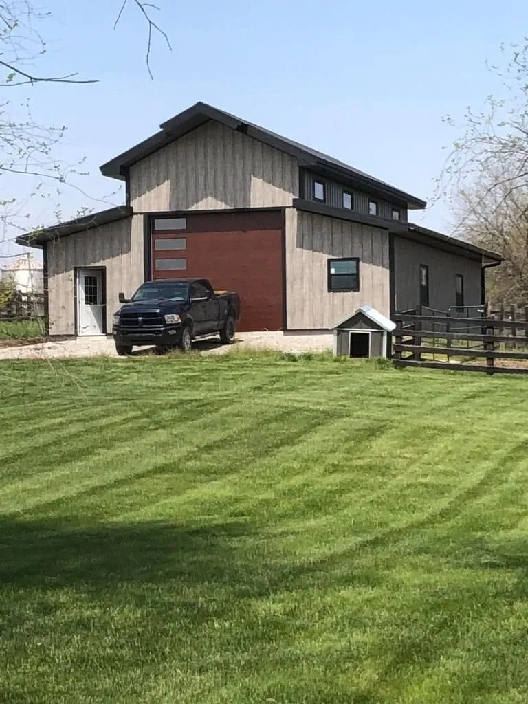 Gray barn with red garage door, black truck parked in front, and dog house on green lawn.