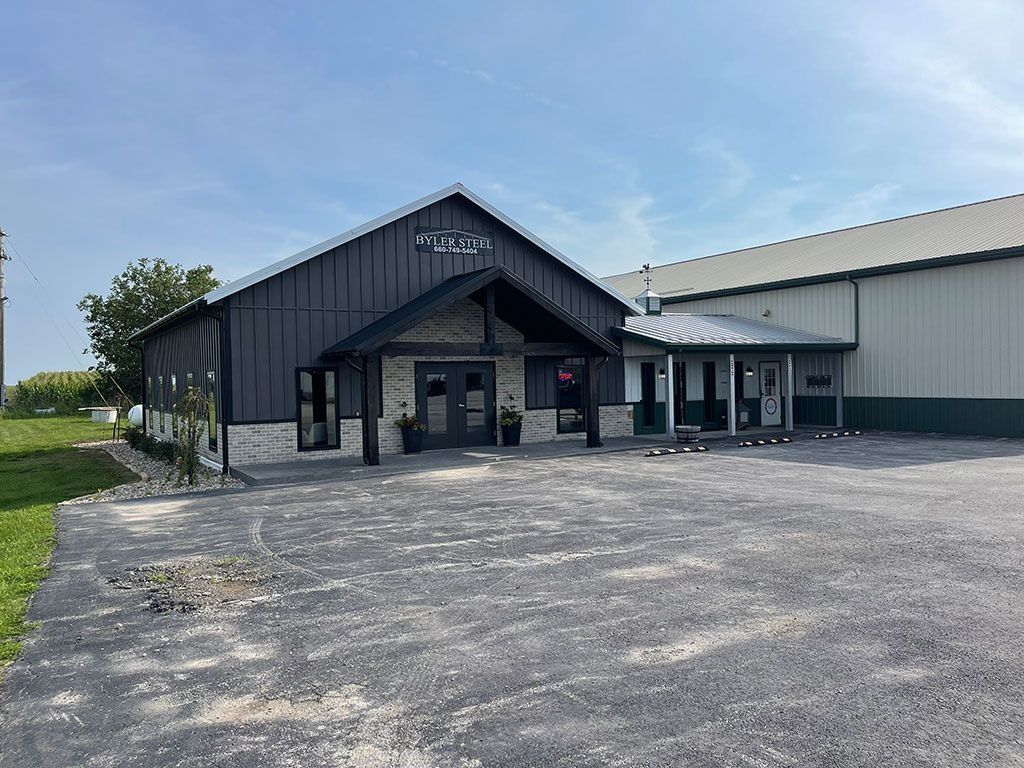 A dark gray building with stone accents and a gravel parking lot on a sunny day.