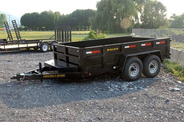 A dump trailer is parked in a gravel lot next to a trailer.