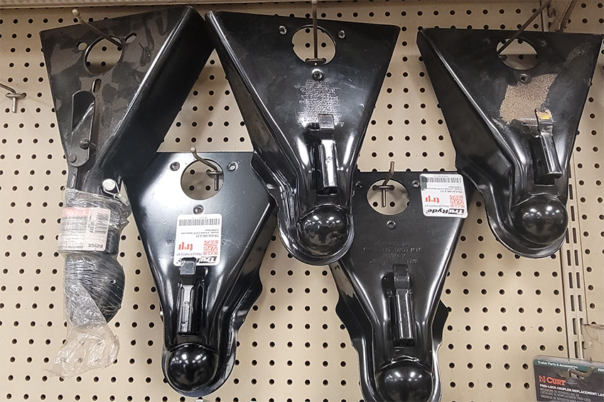 Black trailer tongue couplers hang on a pegboard wall display in a store.