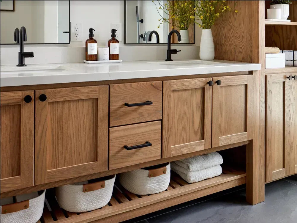 Wooden bathroom vanity with double sinks, black fixtures, and open shelf with baskets.