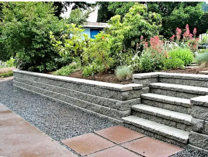 Stone retaining wall and steps leading to a garden with green and pink plants.