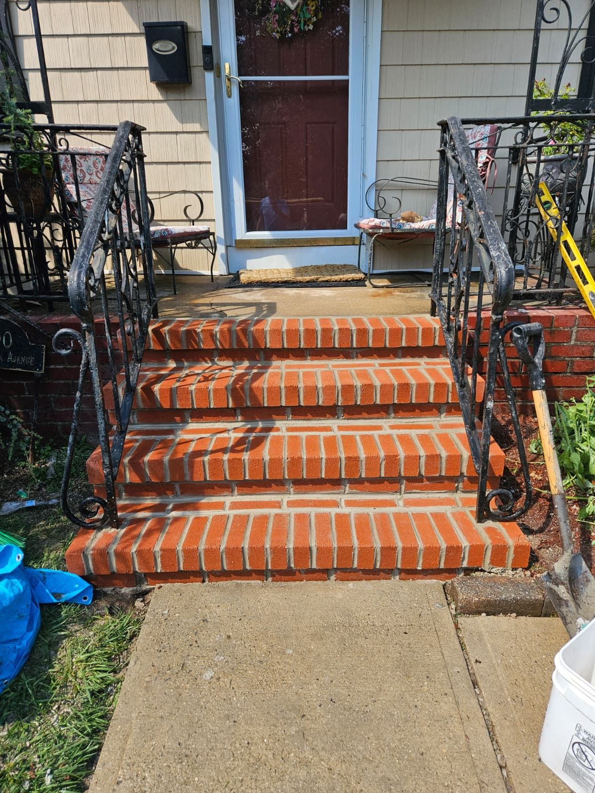 Brick front steps leading to a house with black railings. Concrete walkway.