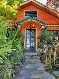 Vibrant orange house with teal trim and lush landscaping, leading to a blue door.