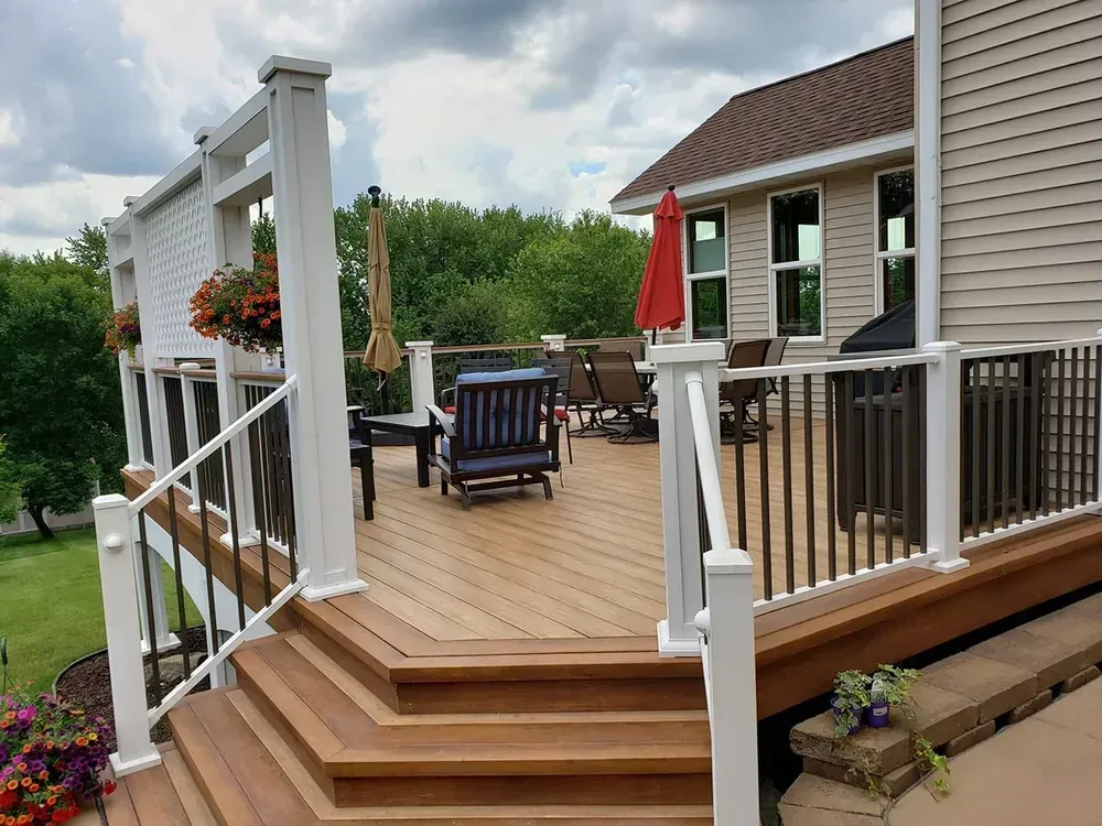 Wooden deck with stairs, railing, and outdoor furniture; house in background.