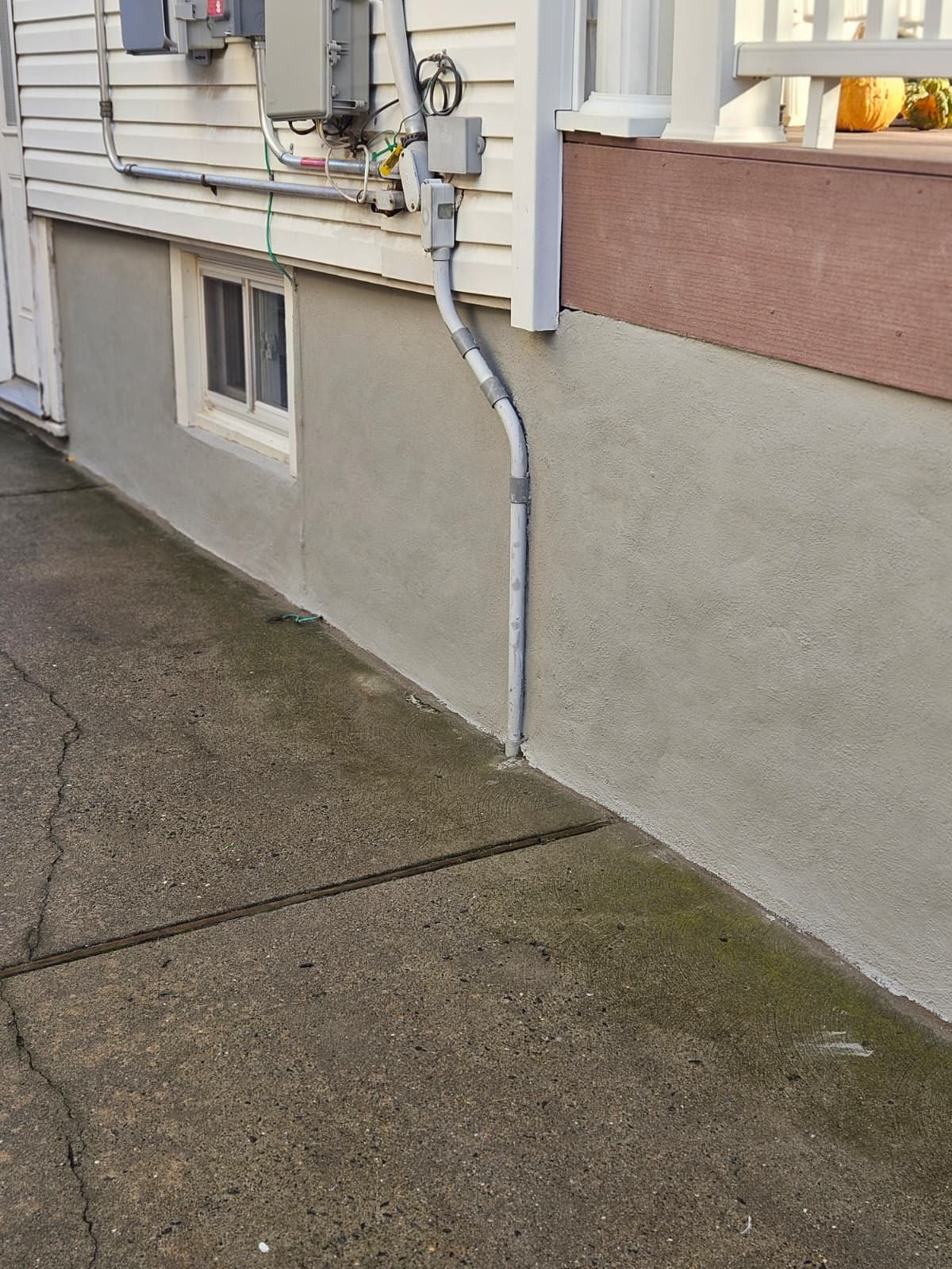 Exterior wall with window and conduit, next to a concrete walkway.