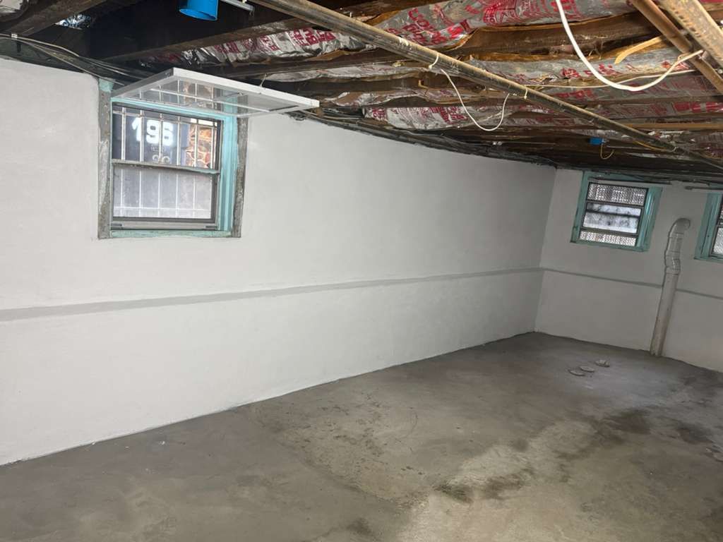Basement interior with gray walls, cement floor, two windows, and exposed ceiling beams.