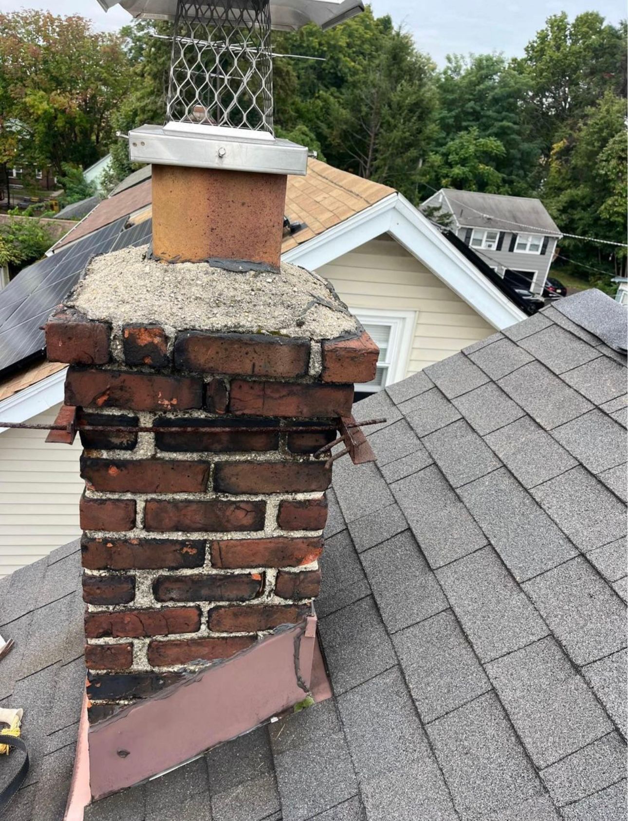 Brick chimney on a shingled roof with a metal cap, surrounding houses visible in the background.