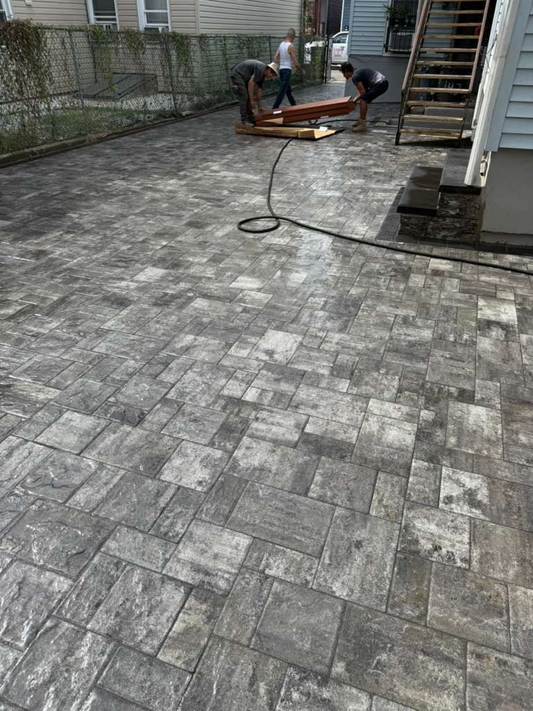 Workers installing paving stones in a gray, patterned driveway. One person holds wooden beams.