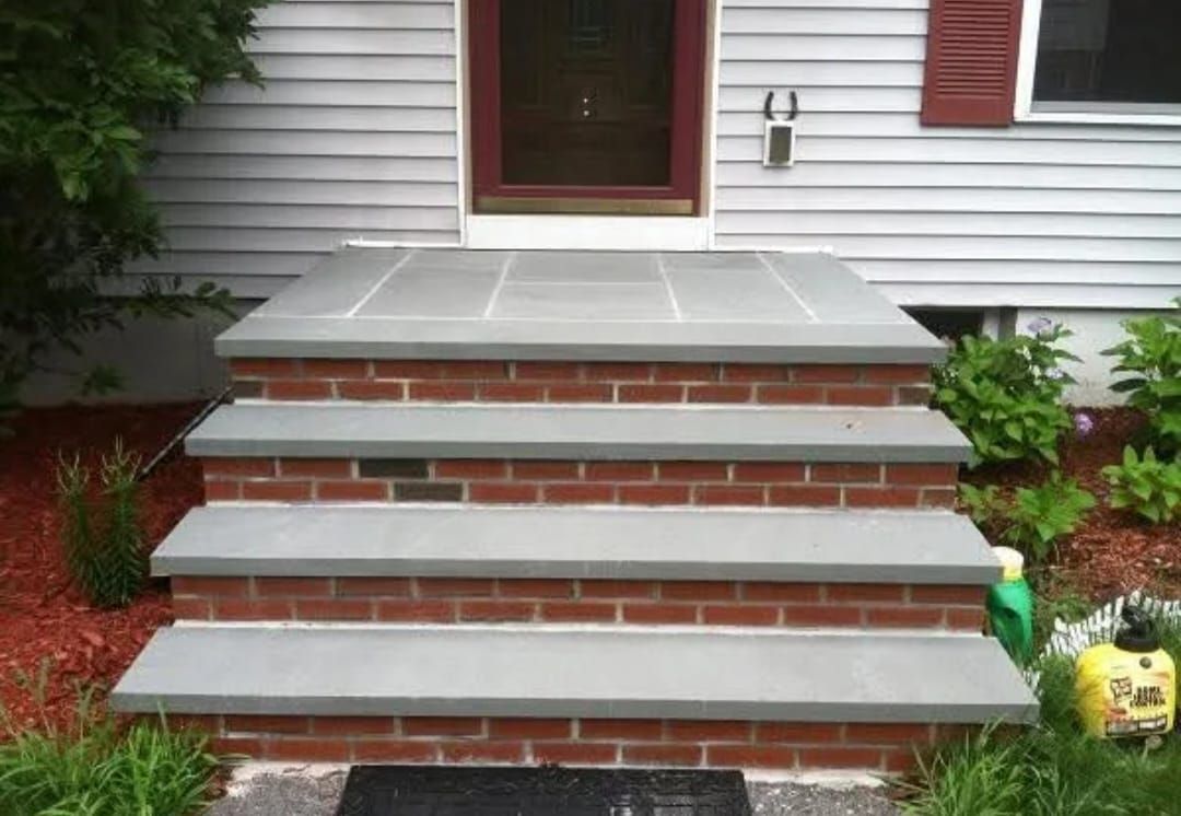 Brick steps leading to a front door with gray stone treads and a red doorframe.
