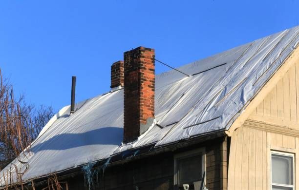House with tarped roof, brick chimneys, and a clear blue sky.