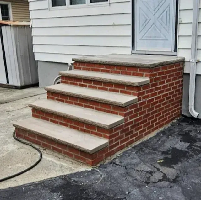 Brick steps leading to a white door, set against a white-sided house. The steps have concrete treads.