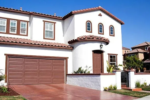 Two-story white stucco house with brown roof, garage door, and trim against a clear blue sky.
