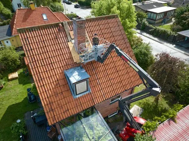 A person on a lift truck working on a chimney on a red tiled roof.