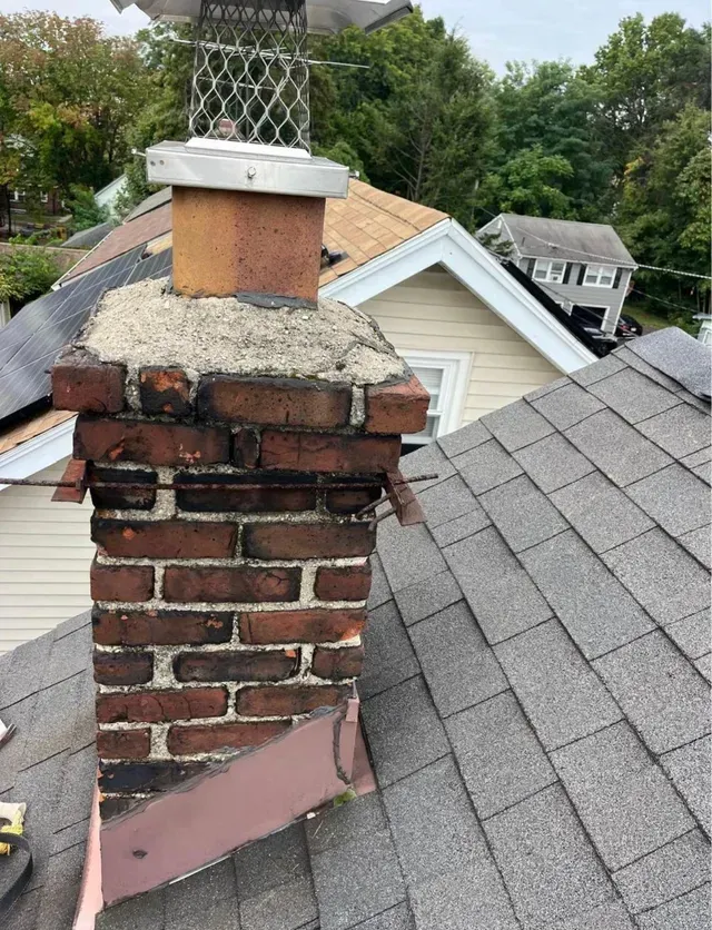 Brick chimney on a shingled roof with a metal cap, surrounding houses visible in the background.