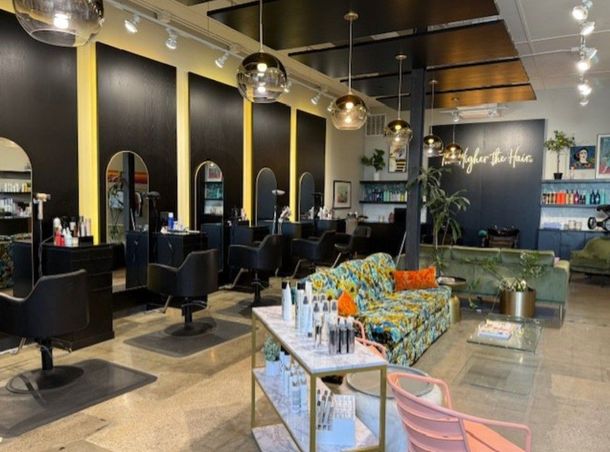 Modern salon interior with black chairs, gold mirrors, and a patterned sofa under warm pendant lights
