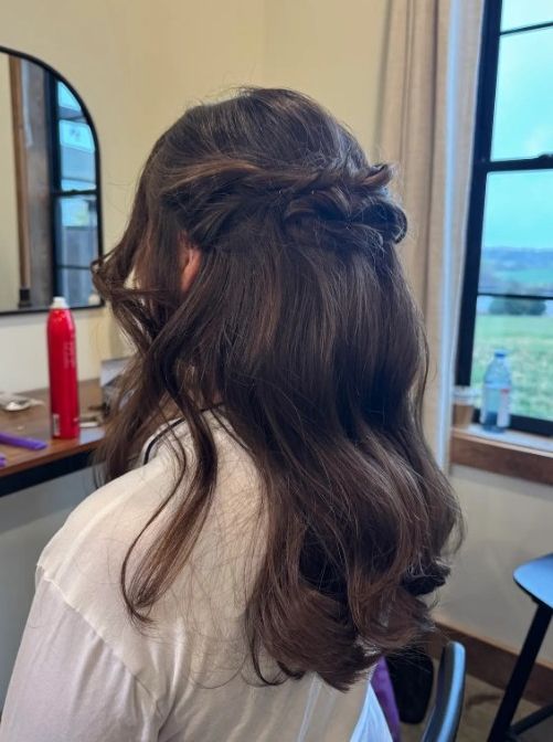 A woman seen from behind with long, dark, wavy hair styled in a half-up, half-down look with twisted side sections.