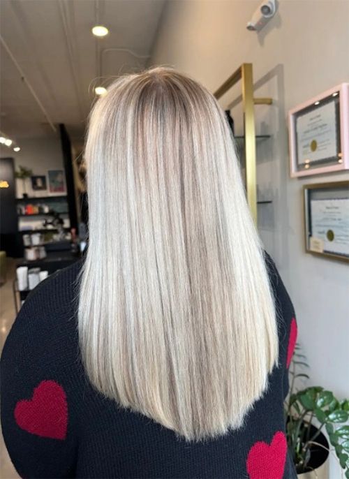 Back view of long, straight, bright blonde hair in a salon setting, worn with a black sweater featuring red hearts.