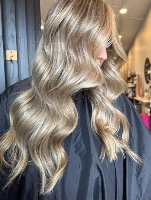 Long, wavy, ash-blonde hair with highlights and soft dimension, viewed from the side in a hair salon.