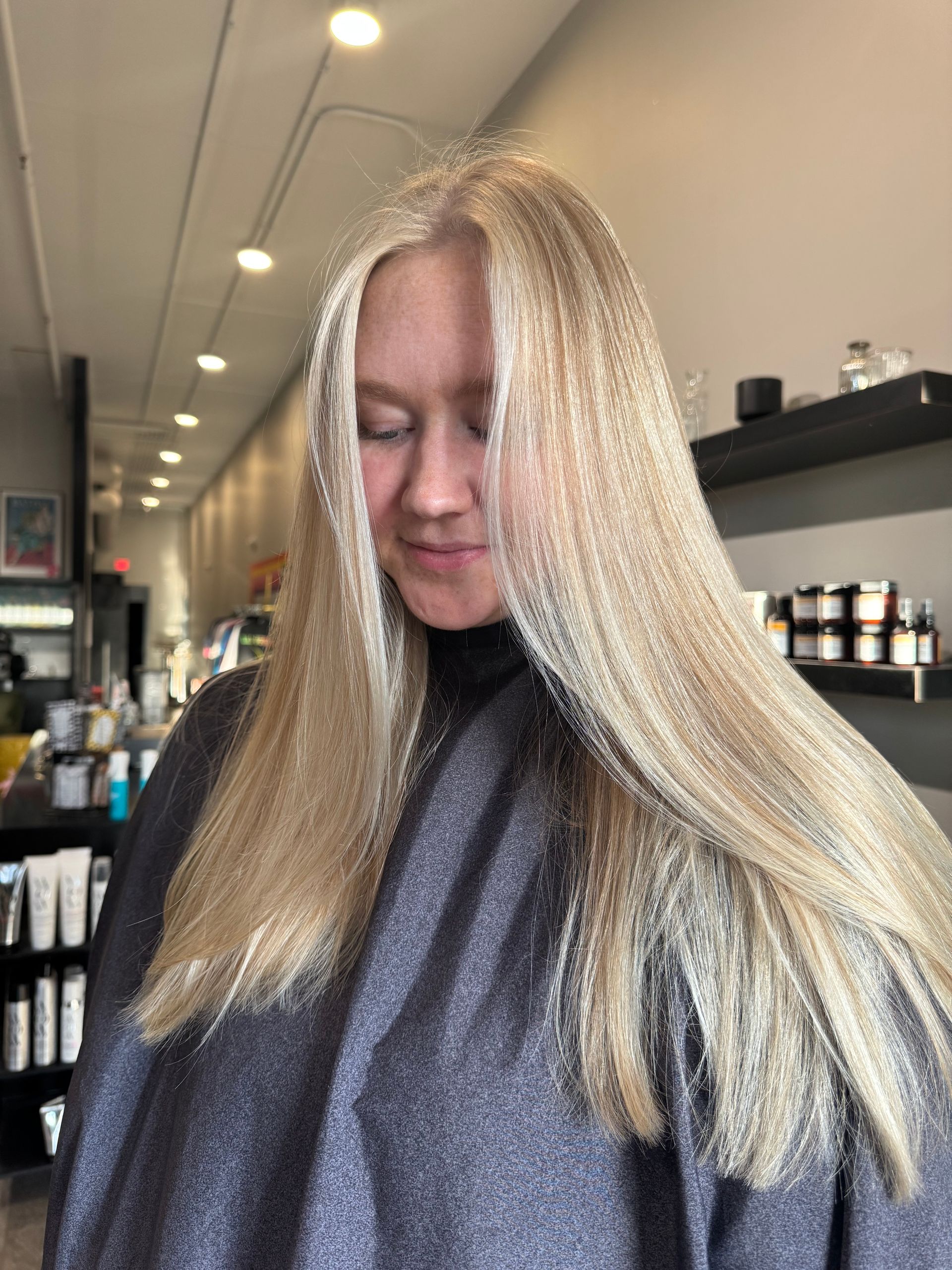 A person with long, straight, bright blonde hair stands in a hair salon.