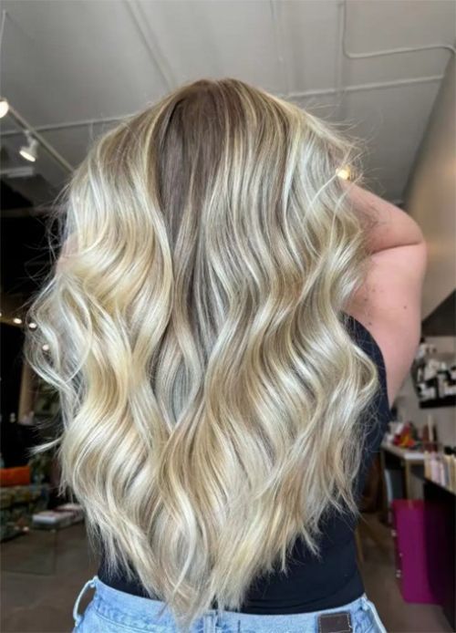 Long, wavy blonde hair styled in a salon, showing dimensional highlights and a dark root shadow.