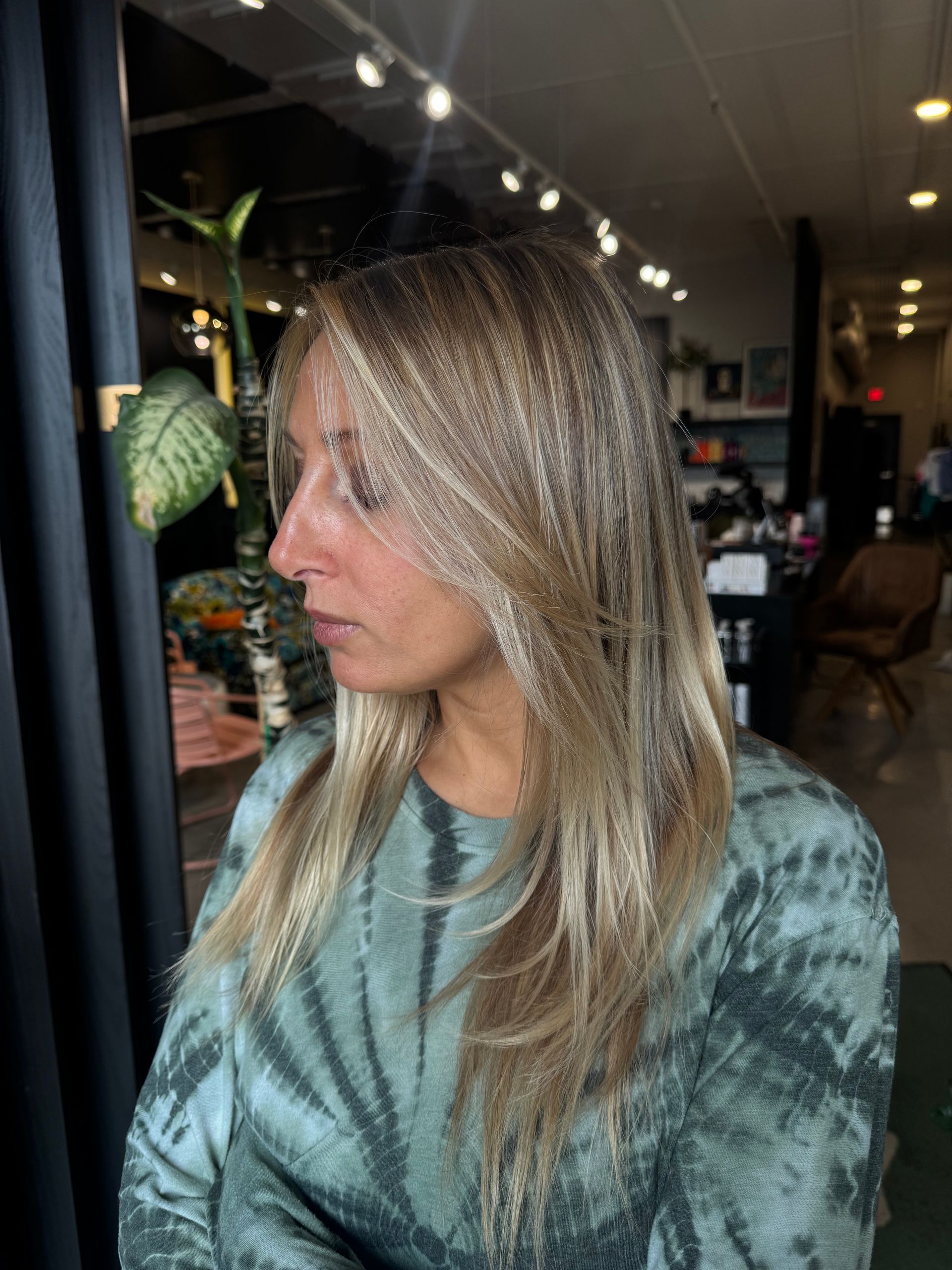A person with highlighted, shoulder-length hair with crimped texture, wearing a green tie-dye shirt in a salon setting.
