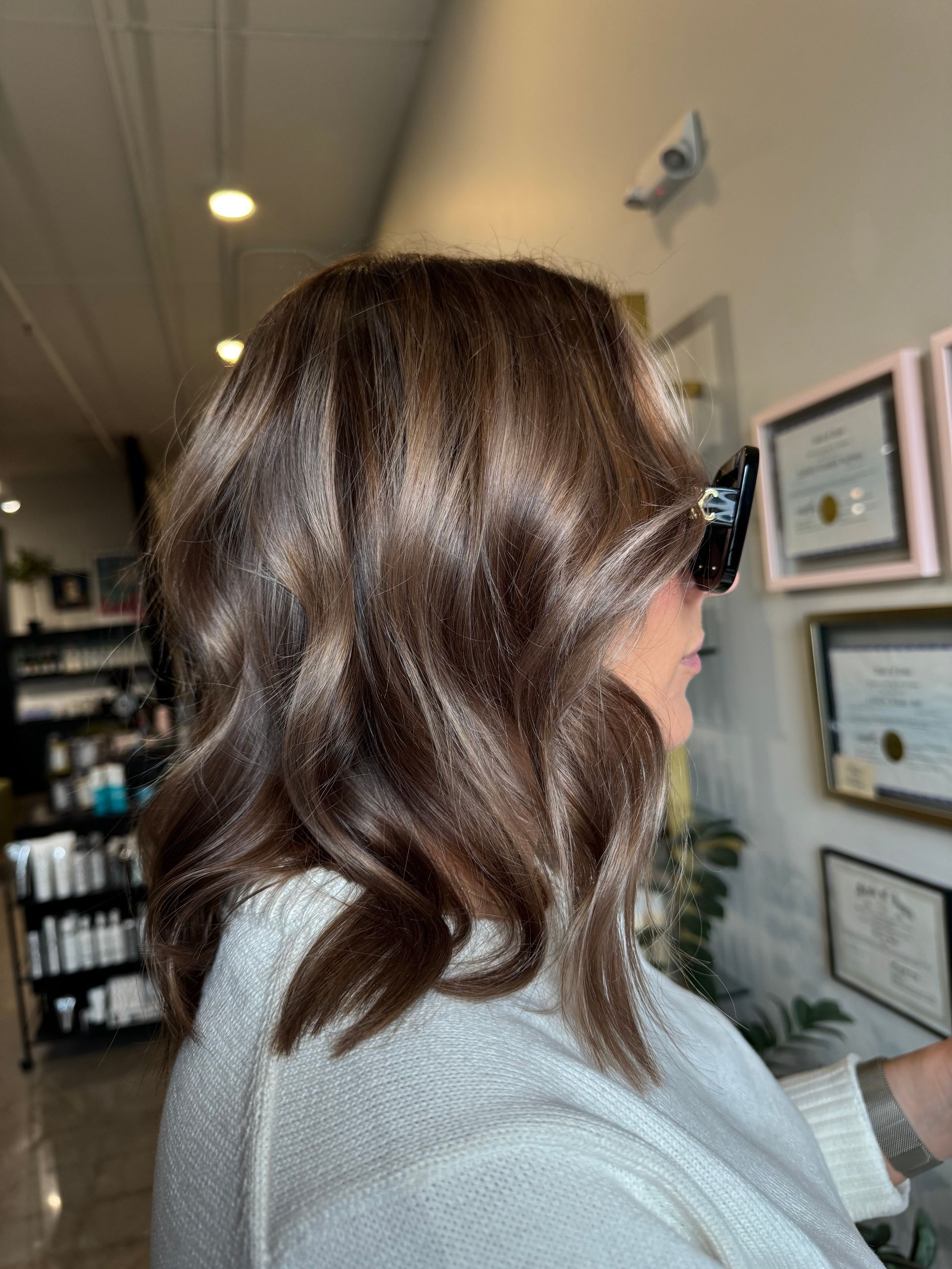 A person with wavy, shoulder-length dark brown hair in a salon setting.