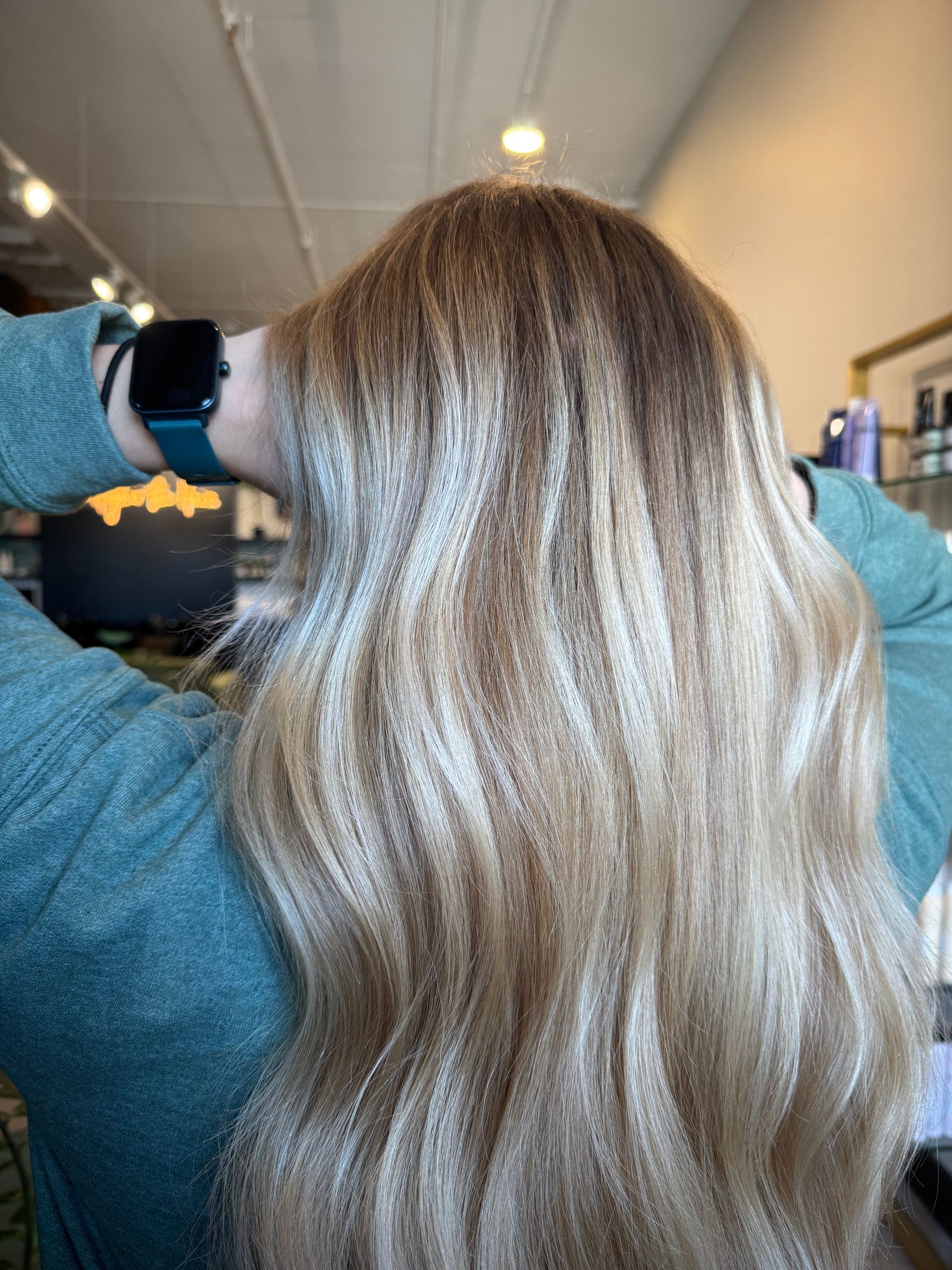 A person wearing a teal sweater with long, wavy hair featuring highlights of blonde, beige, and light brown.