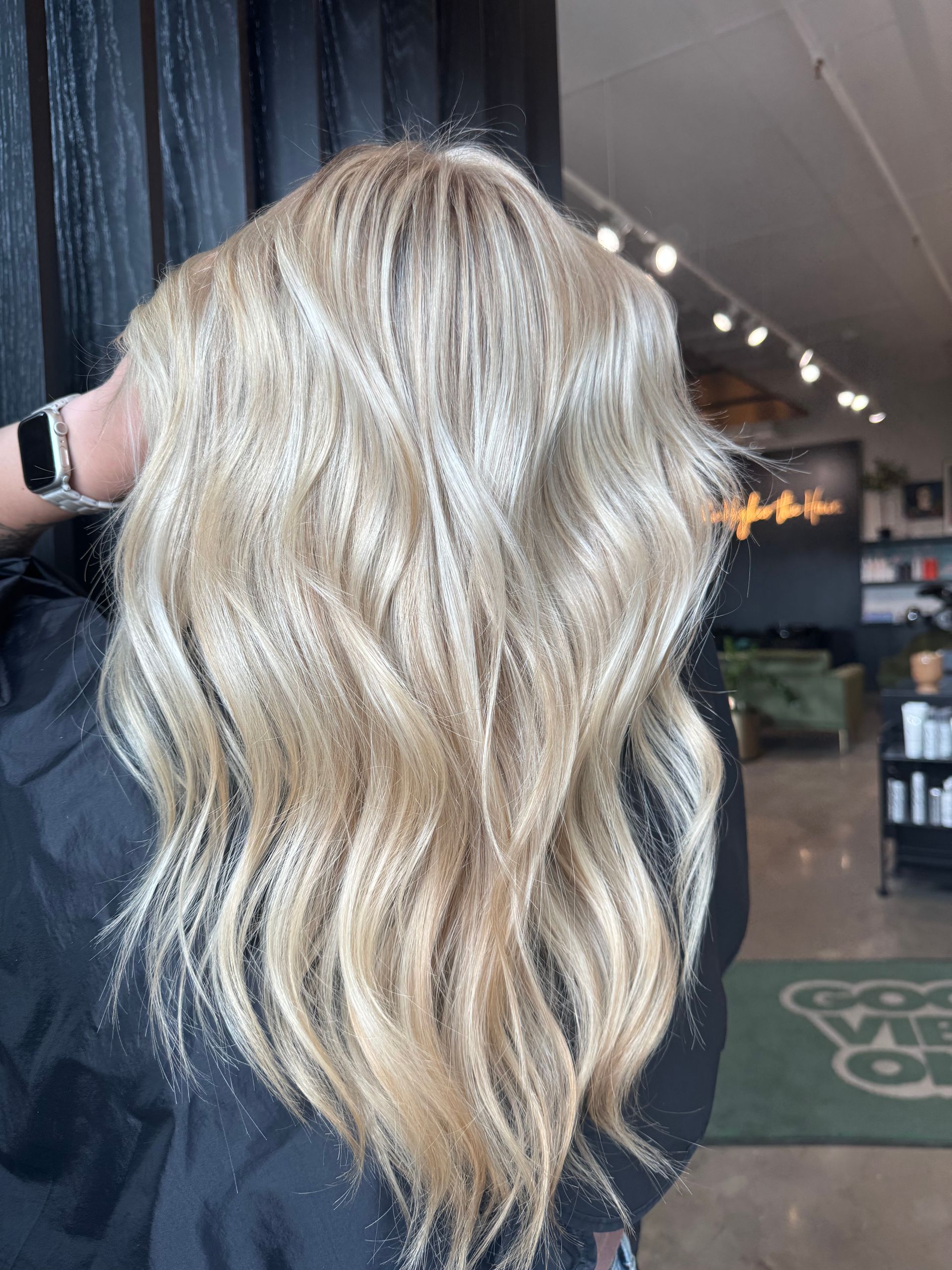 A person with wavy, multidimensional blonde hair styled with highlights, captured in a salon setting.