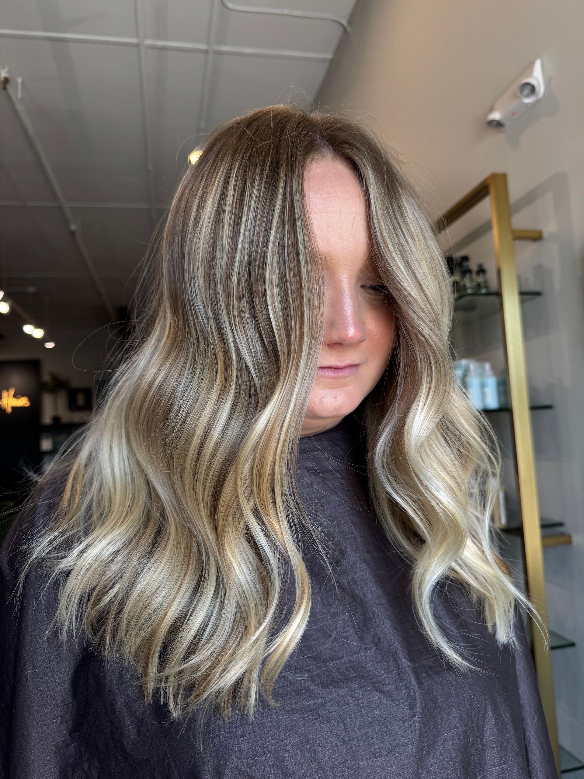 A person with long, wavy blonde highlighted hair styled in a salon setting.