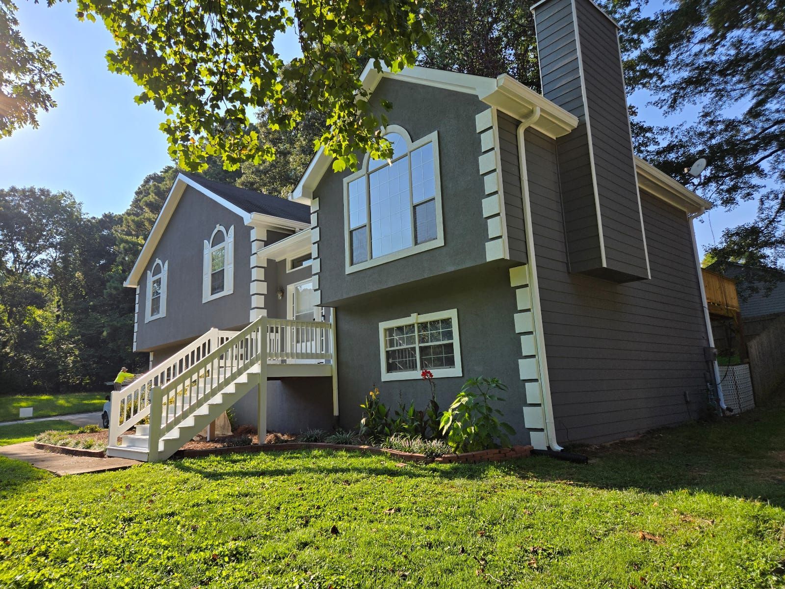 A large house with a lot of windows and stairs is sitting on top of a lush green field.