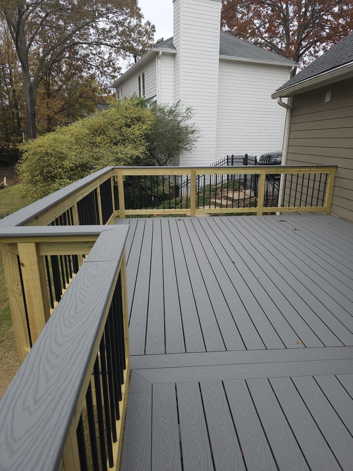 A gray deck with a wooden railing and a house in the background