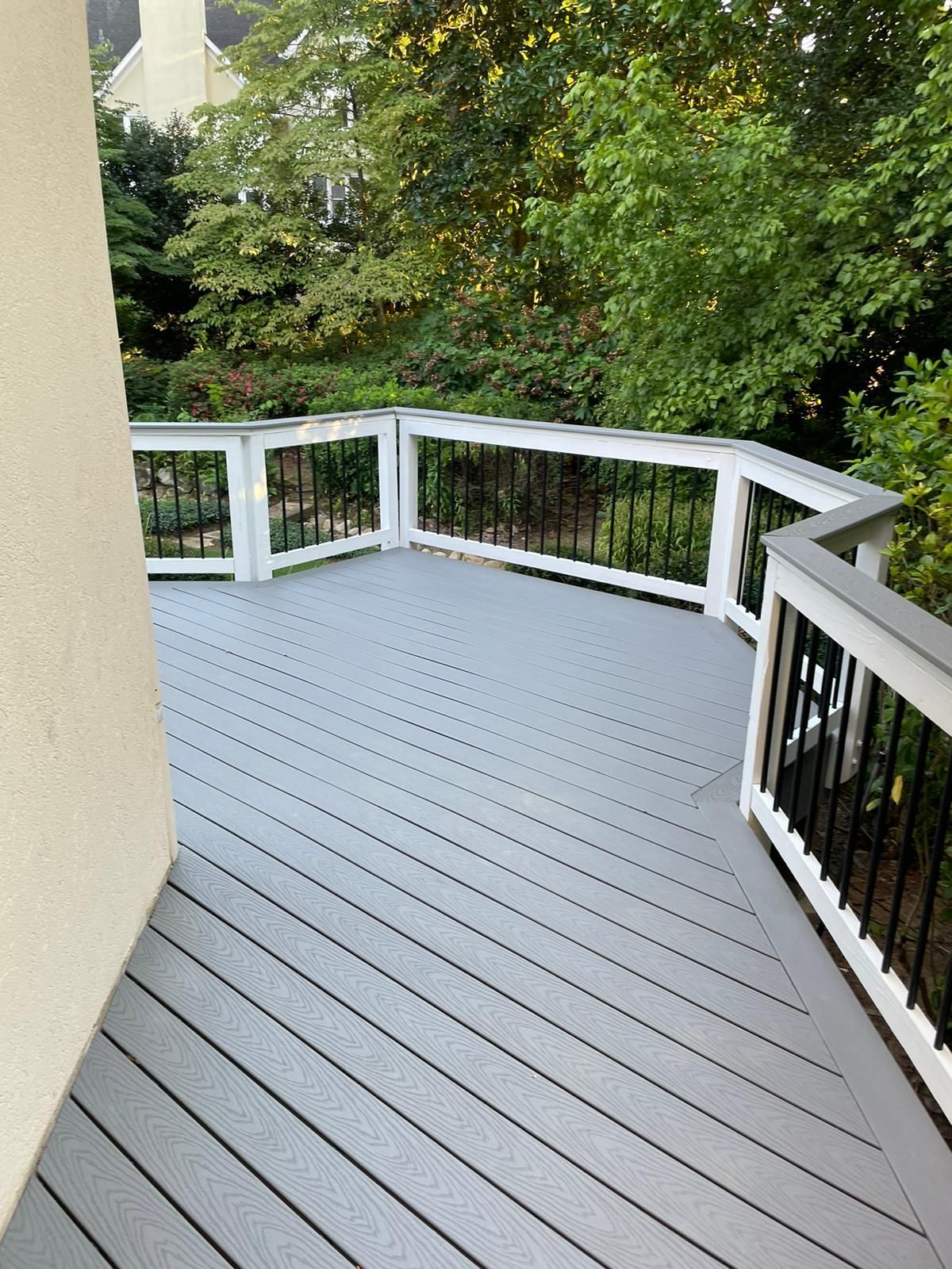 A gray deck with a white railing and trees in the background.