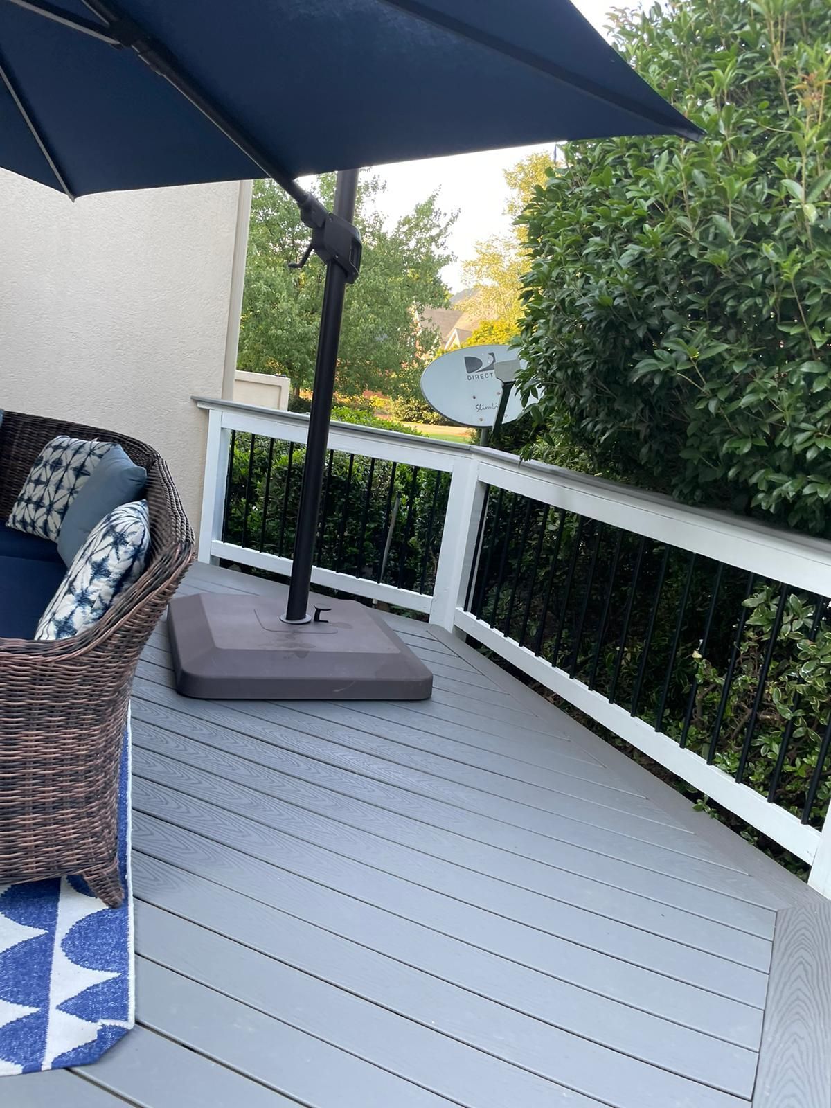 A blue umbrella is sitting on a deck next to a wicker chair.