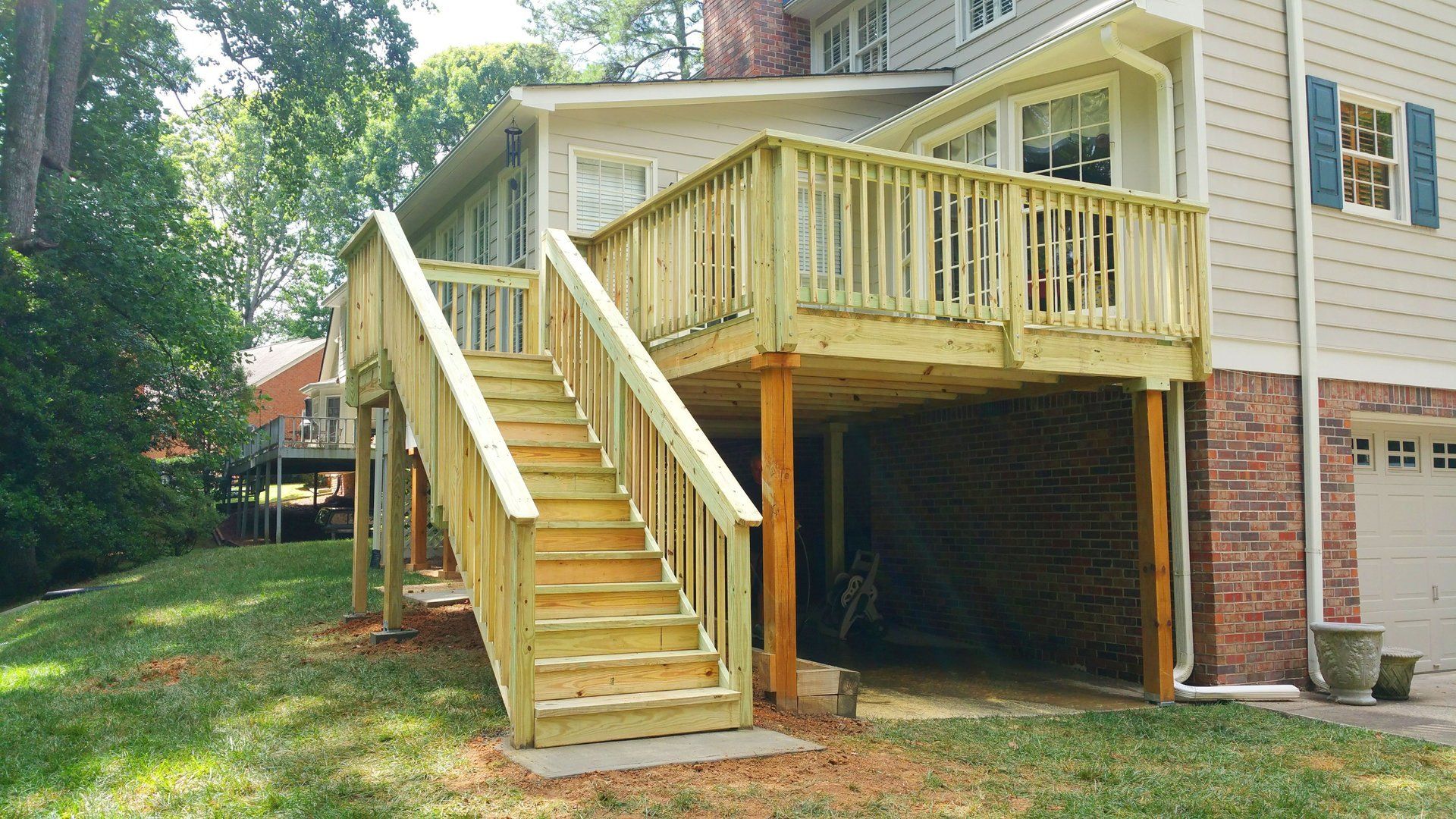 A wooden deck with stairs leading up to it is in the backyard of a house.