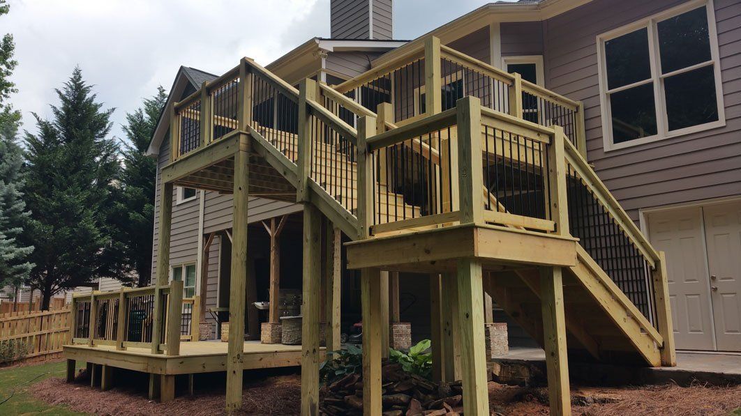 A large wooden deck with stairs leading up to it is in front of a house.