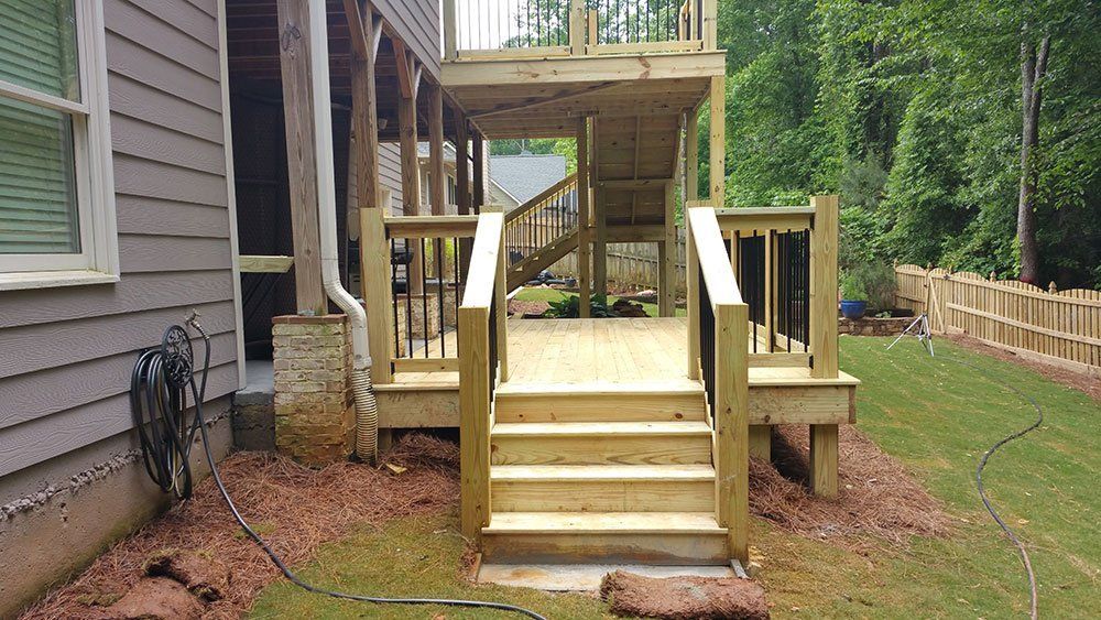 A wooden deck with stairs leading up to it is in the backyard of a house.