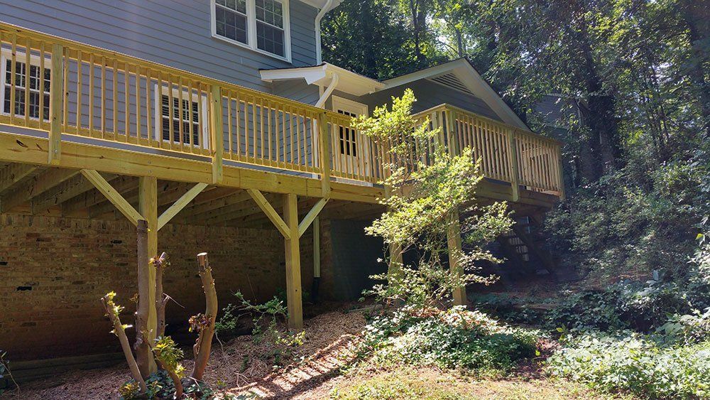 A large wooden deck is sitting underneath a house surrounded by trees.