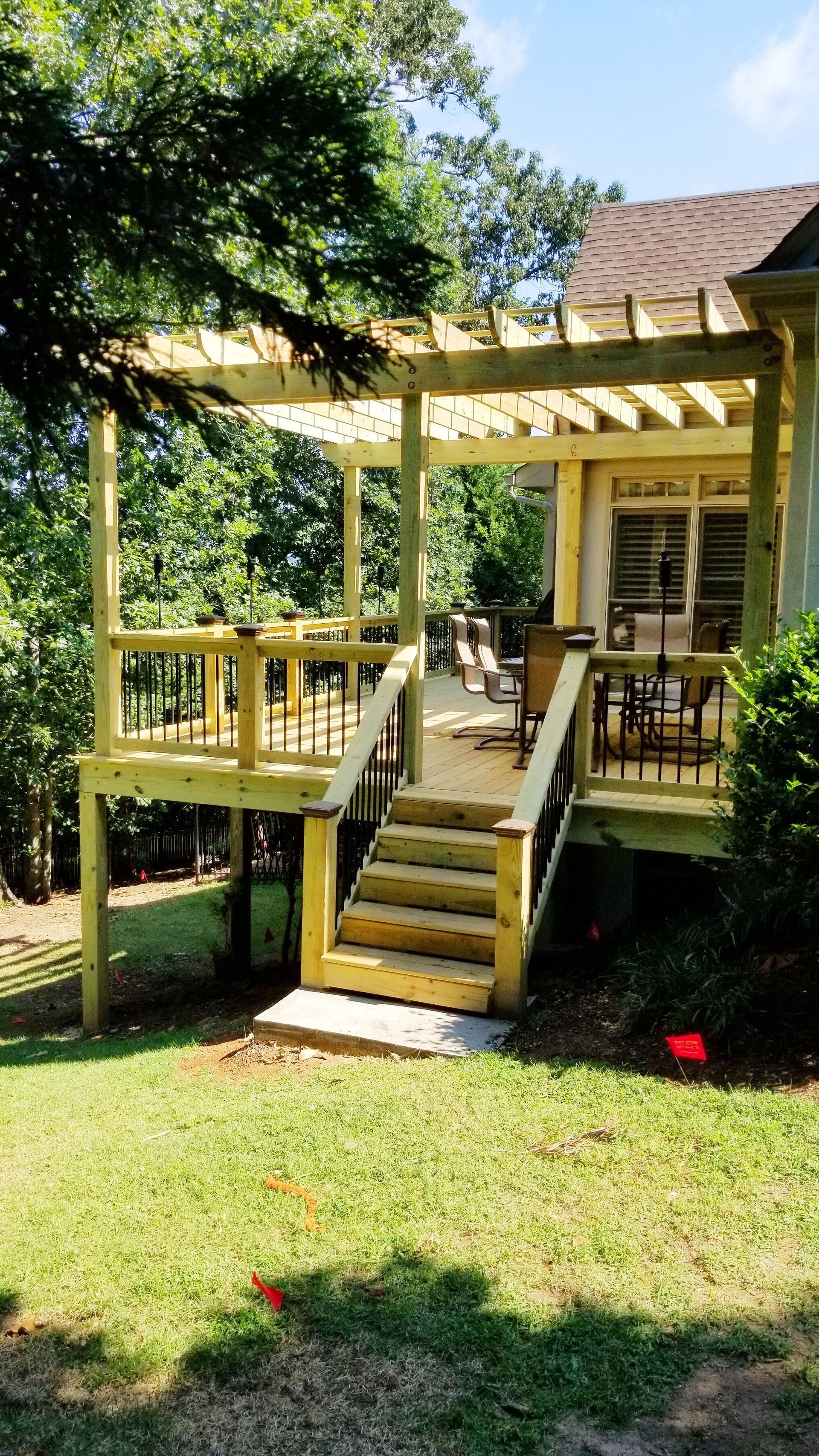 A wooden deck with a pergola and stairs is sitting on top of a lush green lawn.
