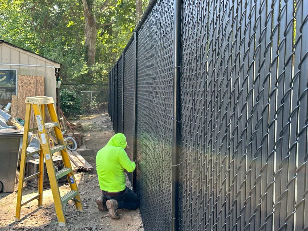 A man is kneeling down next to a chain link fence.