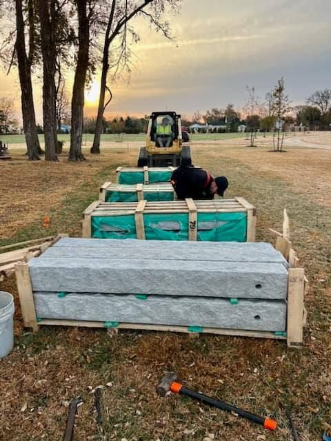 A man is laying on the ground while a forklift moves a bunch of boxes in a field.